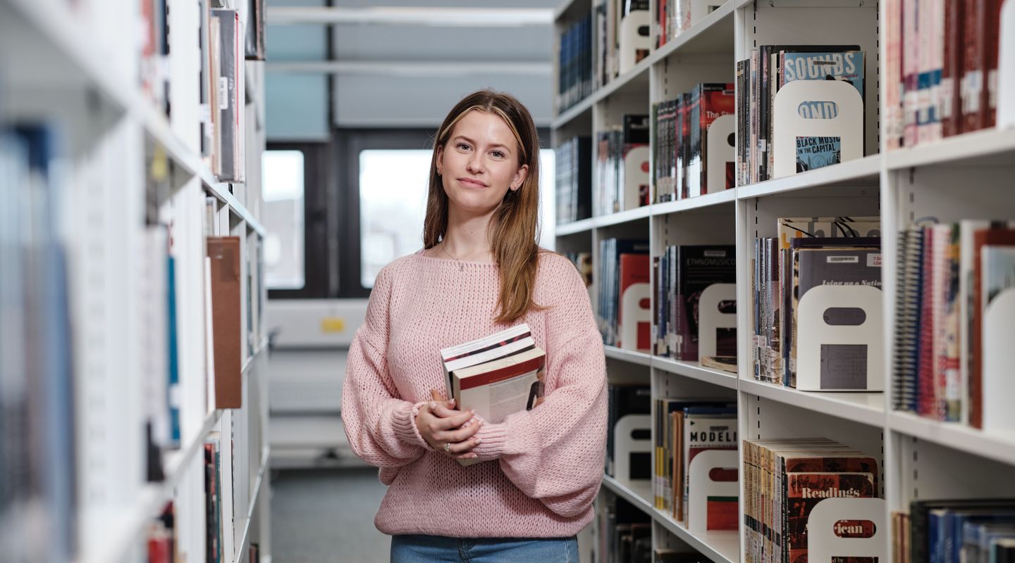 City student smiling at camera in library holding books