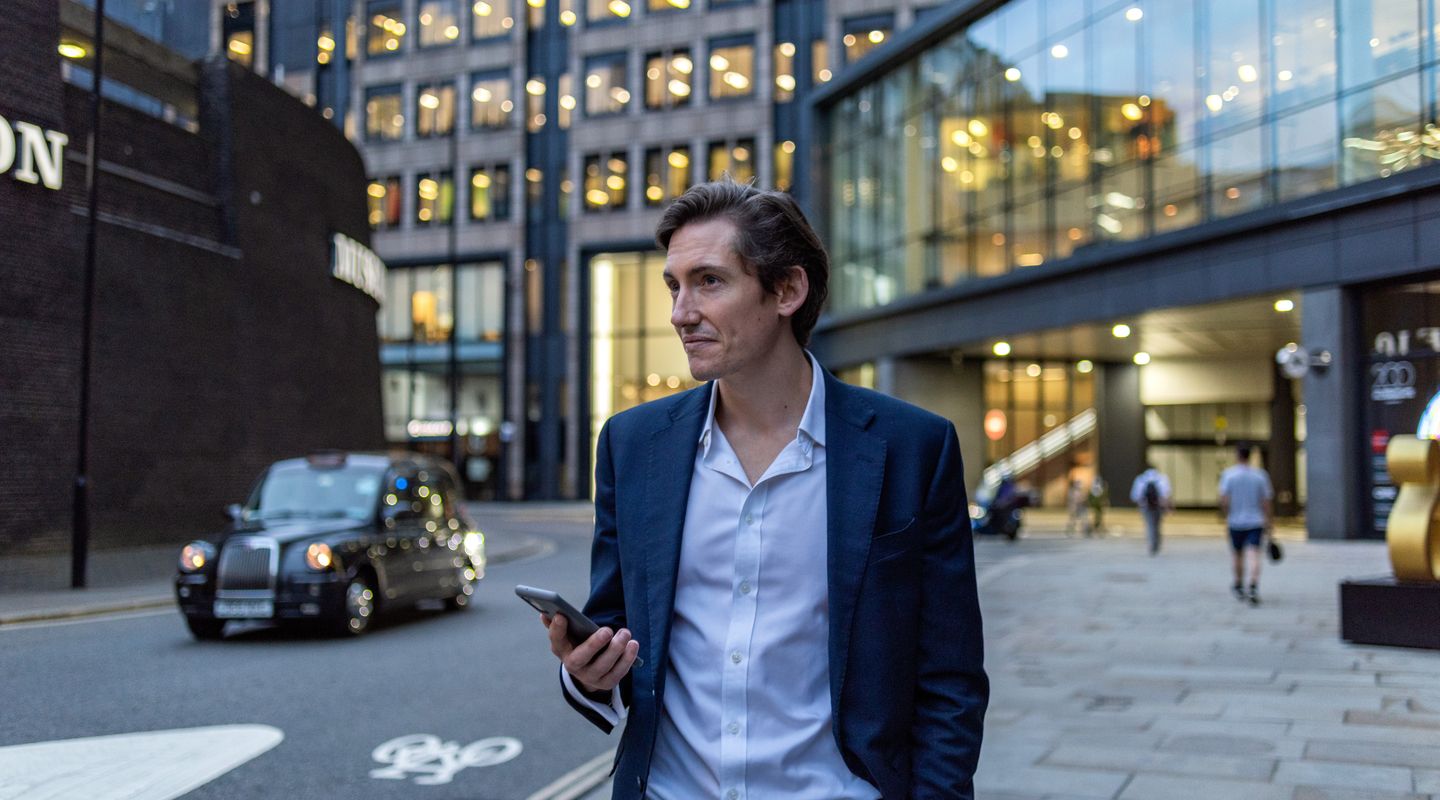 A male MBA student holding a phone in London.