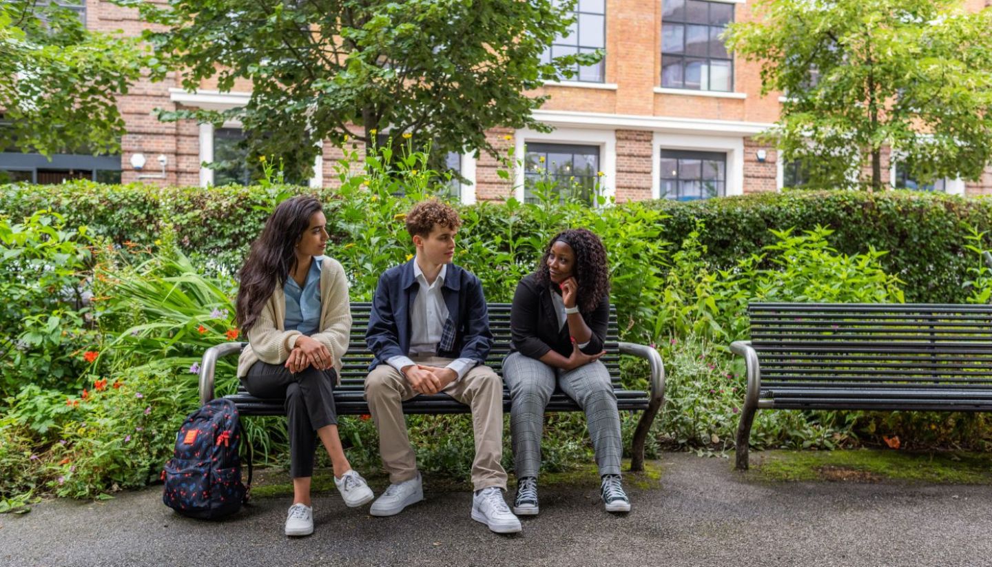A group of students sitting on a bench outside in nature